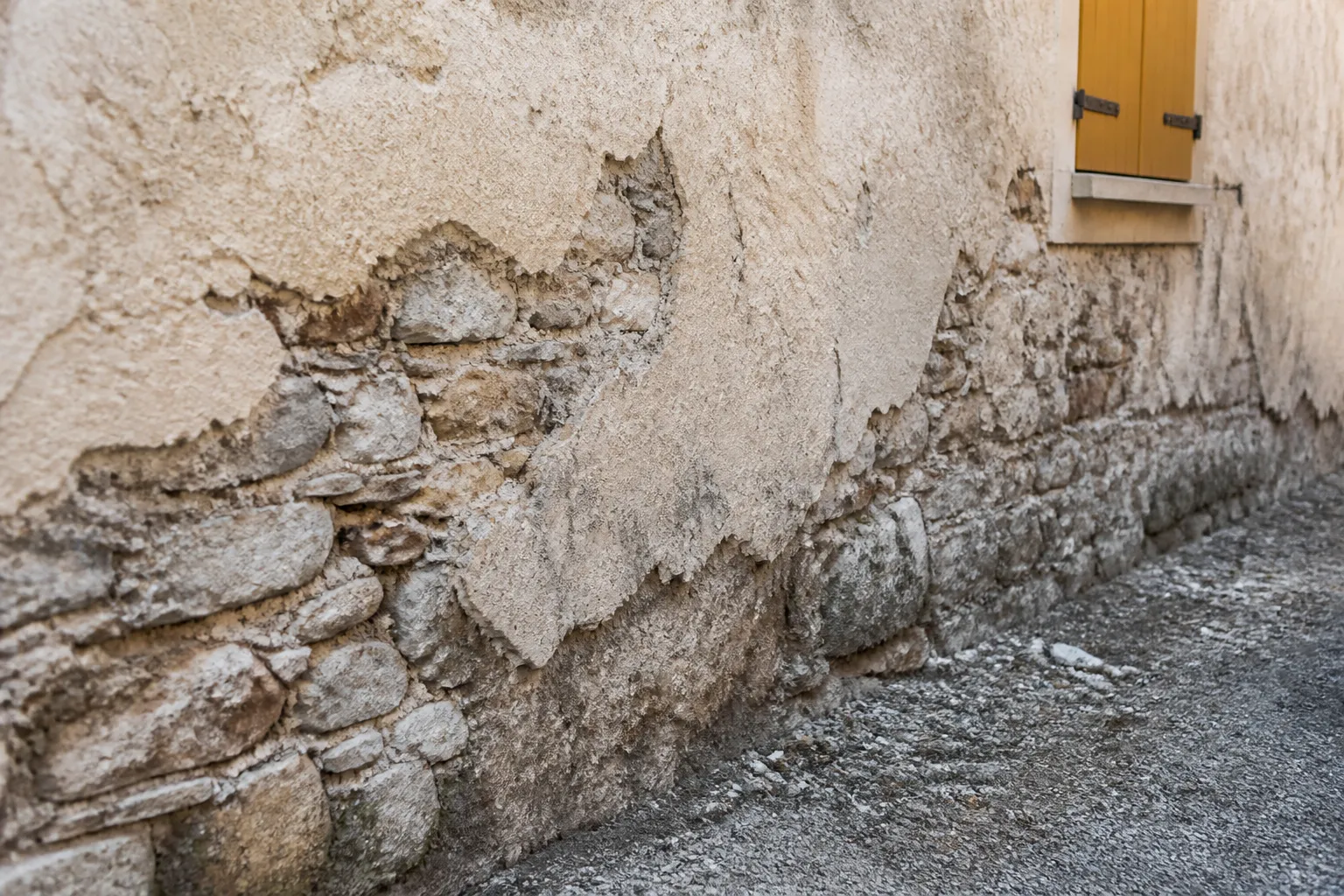 Mur ancien en moellons avec enduit a la chaux degrade au pied