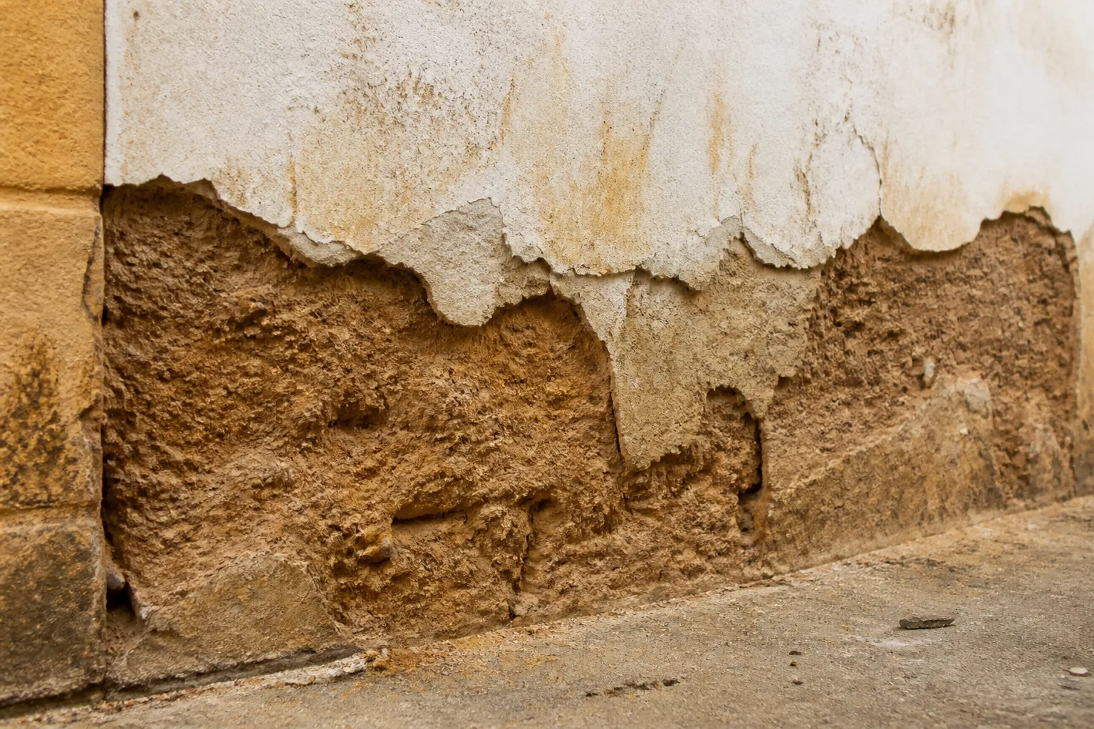 Pied de mur en pise erode avec enduit decolle par plaques